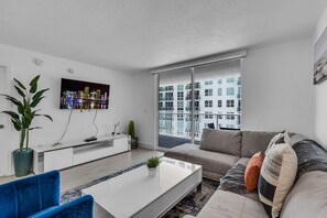 A modern living room with a flat-screen TV, a sofa, a coffee table, and a potted plant. - Elegant 1 BR Retreat in Brickell W/ Free Parking (Miami)