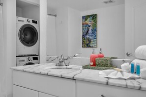 Ein modernes Badezimmer mit Waschmaschine, Waschbecken mit Marmorplatte, großem Spiegel und einem Bild an der Wand.