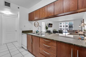A modern kitchen with wooden cabinets, granite countertops, a dishwasher, and a dining area with a sofa and table. - Elegant 1 BR Retreat in Brickell W/ Free Parking (Miami)