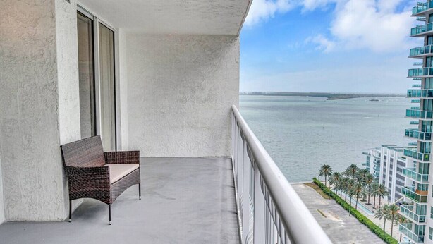 A balcony with a wicker chair, a view of the ocean, and a modern building in the background. - Elegant 1 BR Retreat in Brickell W/ Free Parking (Miami)