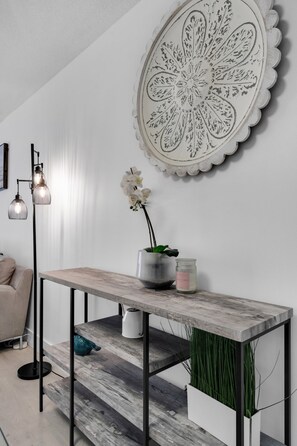 A modern living room with a wooden console table, a potted orchid, a candle, and a decorative wall piece.