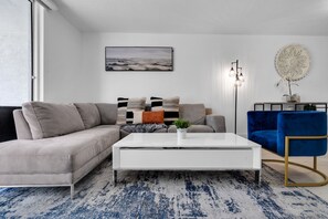 Ein modernes Wohnzimmer mit einem grauen Sofa, einem weißen Couchtisch, einem blauen Sessel und einem gemusterten Teppich.