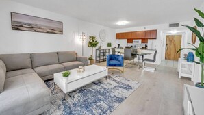 A modern living room with a grey sofa, a white coffee table, and a blue armchair. There is a kitchen area with wooden cabinets and a microwave. - Elegant 1 BR Retreat in Brickell W/ Free Parking (Miami)
