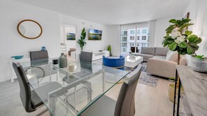 A modern living room with a glass dining table, a sofa, and a large window with a city view. - Elegant 1 BR Retreat in Brickell W/ Free Parking (Miami)