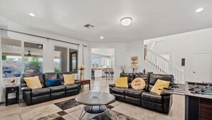 A spacious living room with a fireplace, a dining area, and a kitchen. - Indio Oasis -Pool, Spa, Games & Outdoor Fun (Indio)