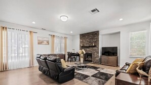 A modern living room with a leather sofa, a dining table, and a fireplace. - Indio Oasis -Pool, Spa, Games & Outdoor Fun (Indio)