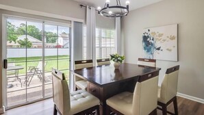 A dining area with a large table, chairs, a chandelier, and a sliding glass door leading to an outdoor patio. - A Getaway on the Gulf Coast for the whole family! (Gulfport)