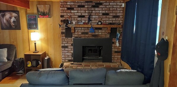 Un salón acogedor con chimenea de ladrillo, un sofá, una lámpara y un retrato de un perro en la pared.