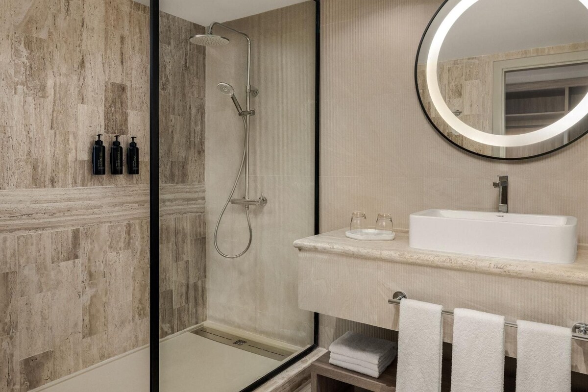 Un bagno moderno con doccia a pavimento, uno specchio rotondo e un lavandino bianco.