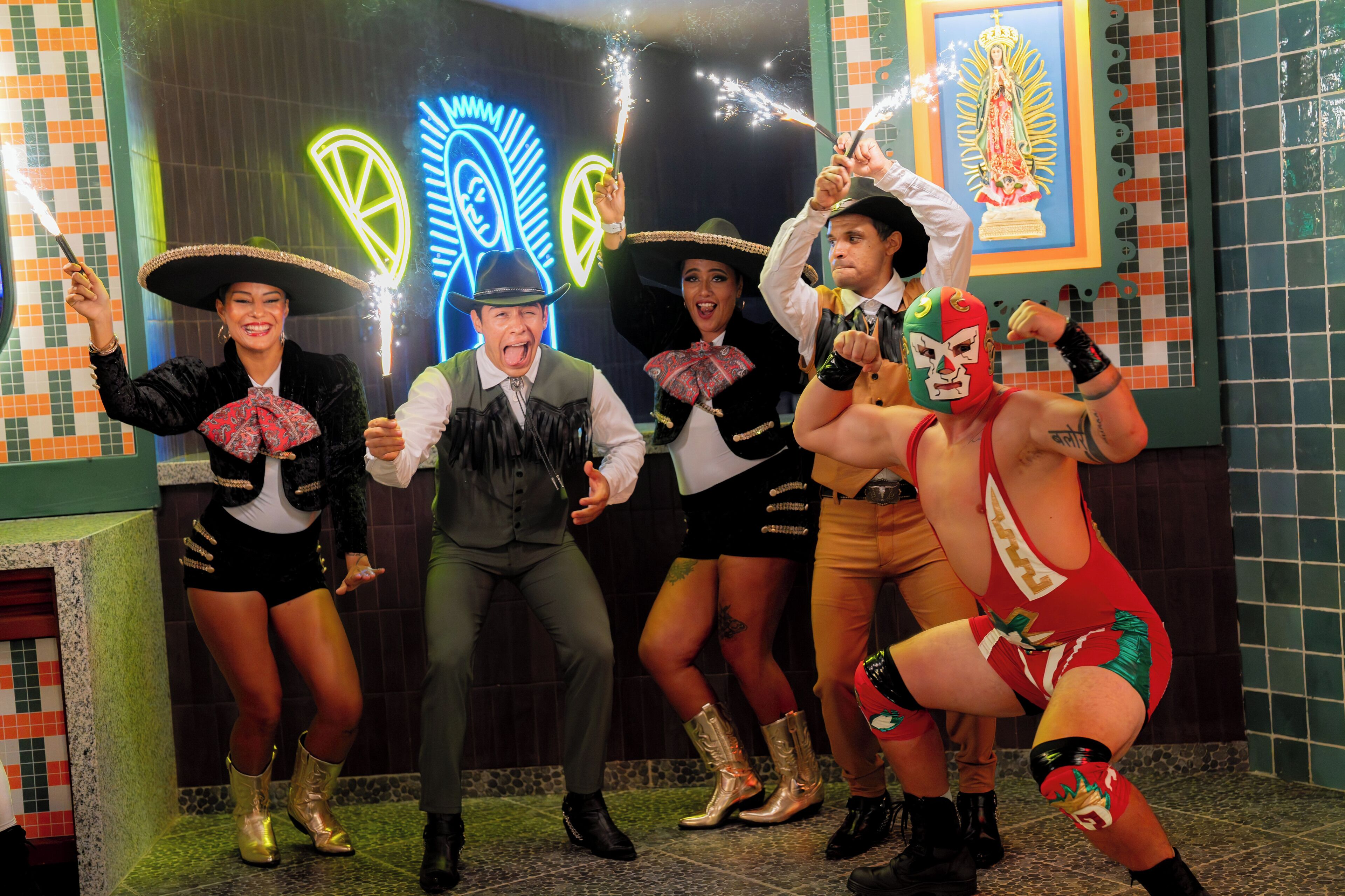 A group of people in festive attire, a neon sign, and a religious icon.