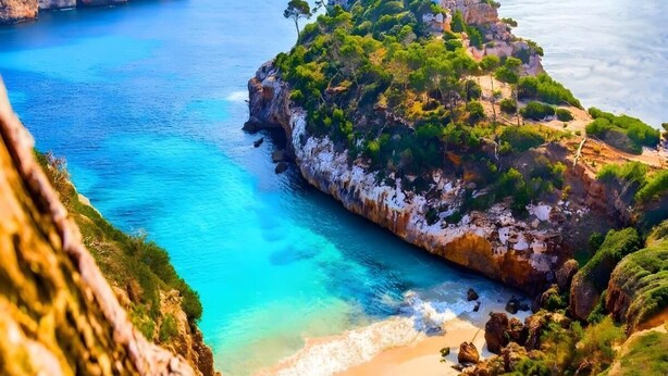 A coastal landscape with a clear blue sea, rocky cliffs, and a sandy beach.
