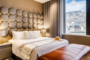 Habitación de hotel con una cama grande, cabecera con diseños circulares, vista a una montaña y un paisaje urbano a través de la ventana.