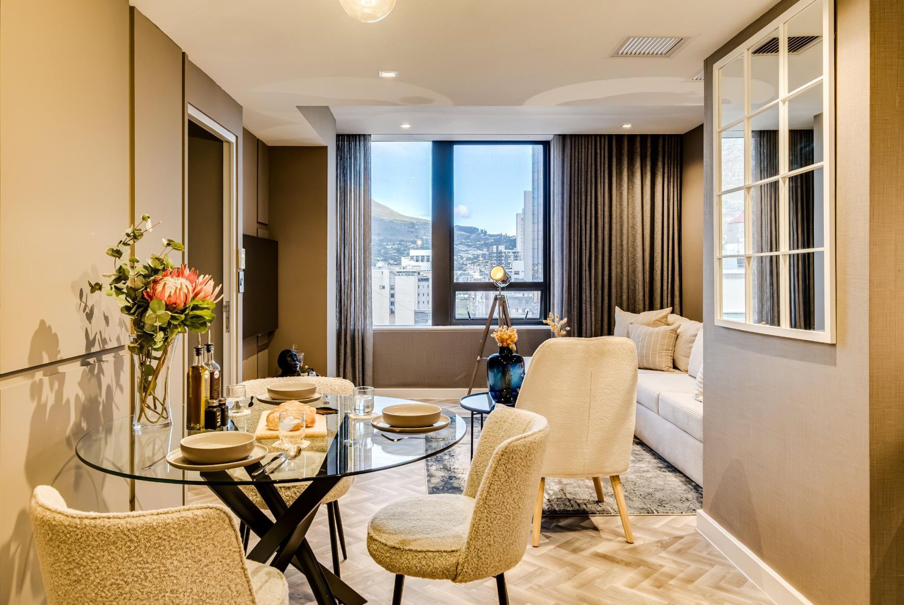 A modern dining area with a glass table, chairs, and a vase with flowers.