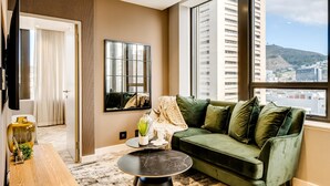 A modern living room with a green sofa, a round black table, and a large window offering a city view. - Trendy 1bed Modern Apt Cape Town City Suite 1601 (Cape Town)