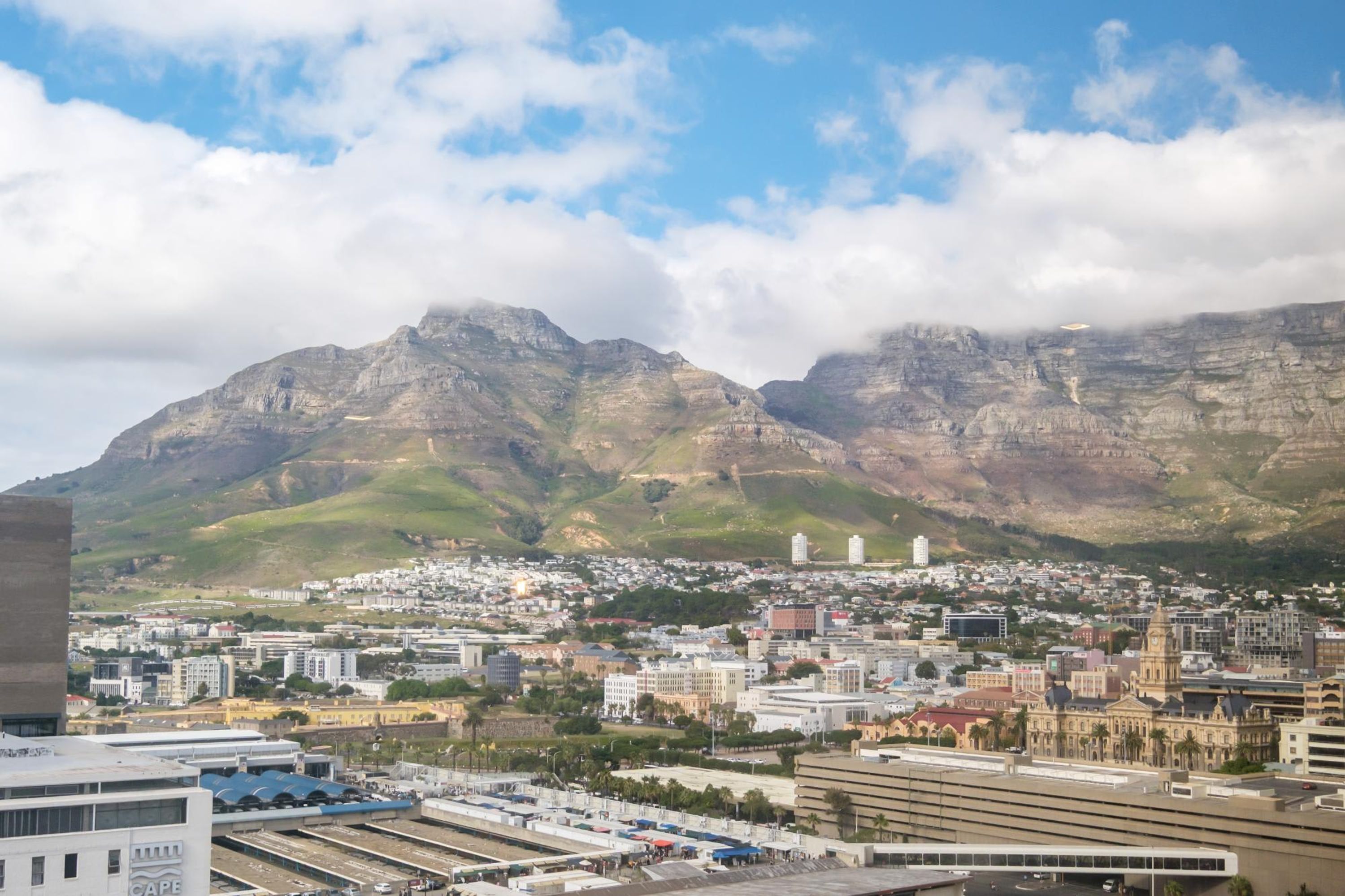 A cityscape with a prominent mountain range in the background, a mix of modern and historical buildings, and a clear sky.