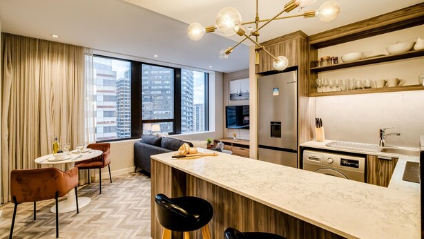 A modern hotel room with a large window, a dining area, a kitchen, and a bar area. - 1bed Apt in Cape Town CBD City Suite 1602 (Cape Town)