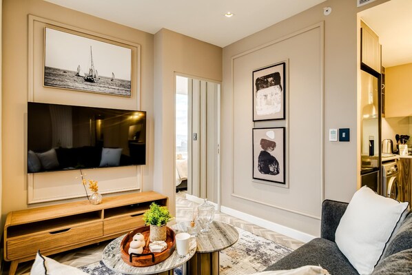 Una sala de estar moderna con un televisor de pantalla plana, una mesa consola de madera, una mesa de centro redonda y un sofá gris.