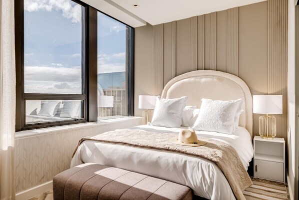 Une chambre d’hôtel moderne dotée d’un grand lit, de deux tables de chevet et offrant une vue sur le panorama urbain grâce à une grande fenêtre.