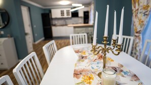 Een eettafel met een tafelkleed met bloemen, witte stoelen en een kandelaar met kaarsen.