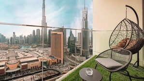 Un balcón con una silla colgante, una mesa de vidrio y vistas a la Marina de Dubái y al Burj Khalifa.