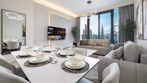 Un comedor moderno con una larga mesa dispuesta para una comida, un sofá con almohadones decorativos y un amplio ventanal con vistas a la ciudad.