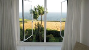 A room with a large window overlooking a coastal landscape, including fields and palm trees.