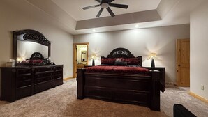 A bedroom with a large bed, a dresser, a mirror, and a ceiling fan.