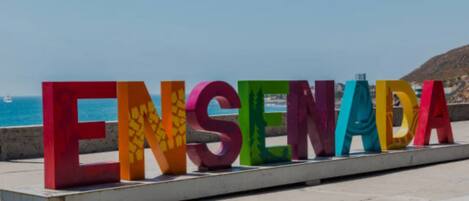 Large colorful letters spelling "ENSEÑADA" on a platform with a coastal background.