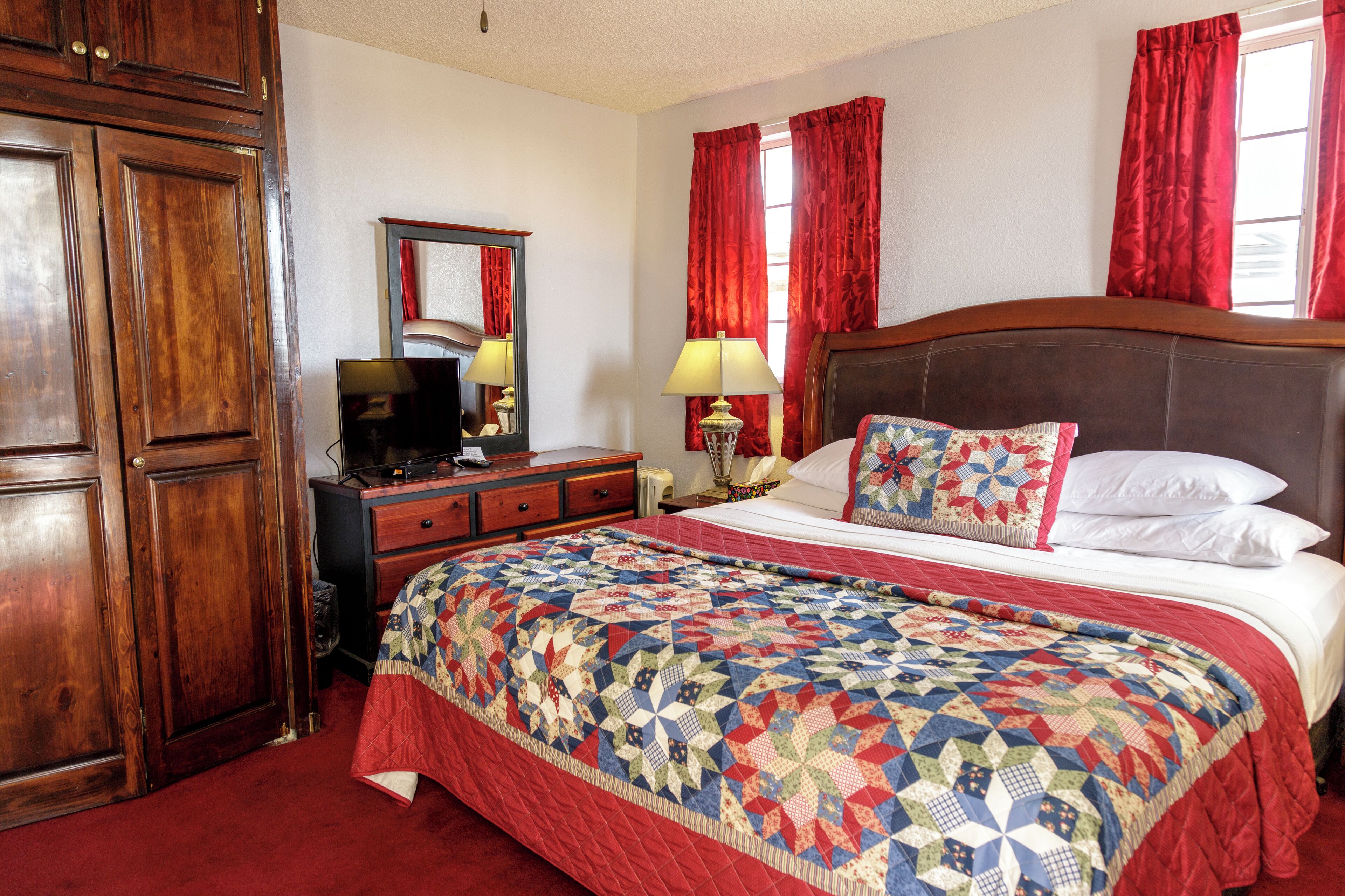 A bedroom with a large bed, wooden wardrobe, a desk with a lamp, and a mirror.