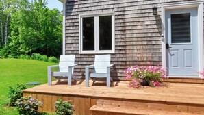 Ein zweistöckiges Haus mit einer Holzterrasse, zwei weißen Stühlen und einem Blumenkasten.