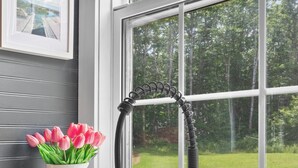 Eine Küche mit einem schwarzen Spülbecken, einer weißen Karaffe mit rosa Tulpen und einem Fenster mit Blick auf Grünflächen.