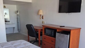 A hotel room with a bed, a desk with a computer, a TV, a lamp, a mirror, and a bathroom with a sink and shower. - Coratel Inn & Suites by Jasper Anthony- 1 King Bed Non-Smoking (Anthony)