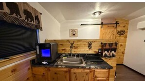 A kitchen with wooden cabinets, a black countertop, a sink, a stove, and a wall-mounted clock. - Bear Cabin (Noble)