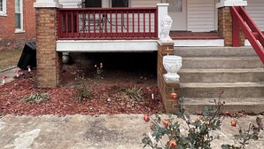 A two-story house with a red front porch, brick foundation, and a small garden with mulch and flowers. - Charming 2-bedroom apartment in beautiful Belleville with WiFi (Belleville)