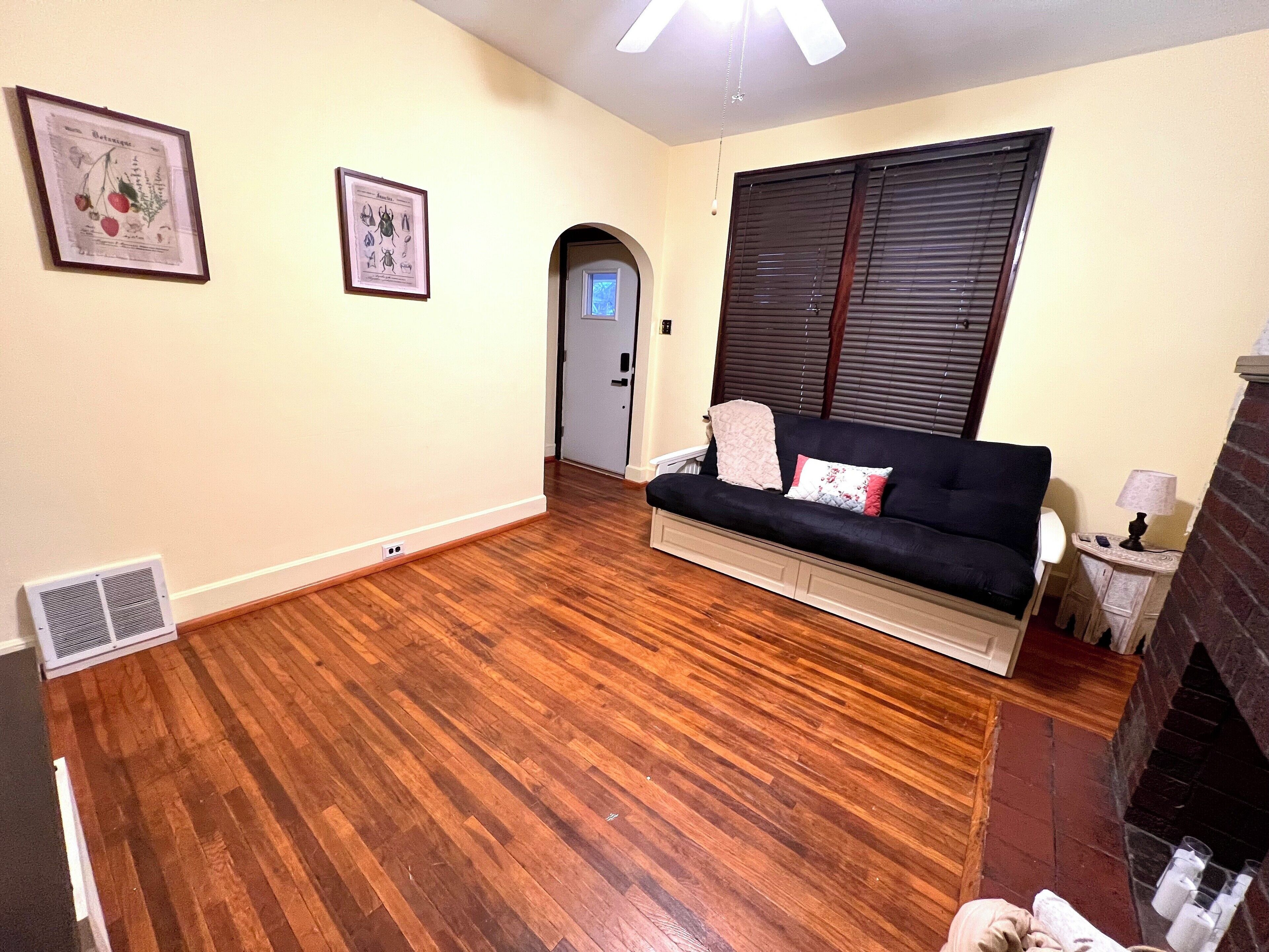 A living room with a dark blue sofa, a fireplace, wooden flooring, and two framed botanical prints on the wall.