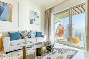A modern living room with a sofa, a glass-top coffee table, and a large window with a view of buildings. - Beachfront 1BR Oasis & Stunning Views By Elie Saab (Dubai)