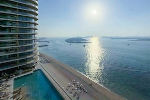 A high-rise hotel with a pool and beach area, overlooking a calm body of water with boats. - Beachfront 1BR Oasis & Stunning Views By Elie Saab (Dubai)