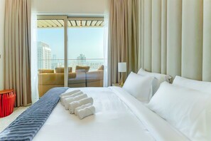 Une chambre d’hôtel avec un grand lit, une vue sur la ville depuis la fenêtre et un balcon aménagé avec des sièges.