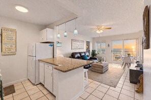 A modern kitchen with a central island, a dining area with a view, and a living room with a sofa and a ceiling fan.
