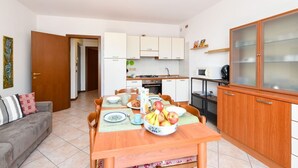 A compact living space with a dining table set for breakfast, a kitchenette, a sofa, and a cabinet with glass doors. - Casa Vuvi - Two-room apartment very close to the beach. (Toscolano Maderno)