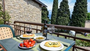 A table with food, wine, and a view of trees and a building. - Casa Vuvi - Two-room apartment very close to the beach. (Toscolano Maderno)