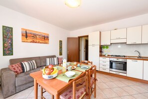 A modern kitchen with white cabinets, a dining table with chairs, and a sofa with patterned cushions.