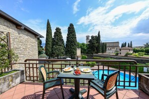 A terrace with a table and chairs, a swimming pool, and a stone building in the background.
