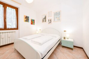 A bedroom with a bed, a nightstand, a window with curtains, and wall art.