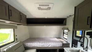 A compact RV interior with a bed, kitchenette, and seating area. - NEW 2025 RV, 1 Bedroom WiFi AC in Serene Winterport with Coast and Bangor nearby (Winterport)