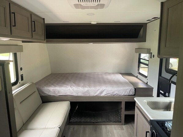 Een ruimtelijk ingericht camperinterieur met een bed, een klein keukenblok en een raam.