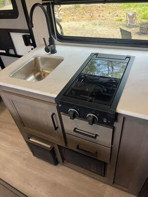 Een compacte kitchenette met een RVS spoelbak, een zwarte Furrion kookplaat en een kleine oven.