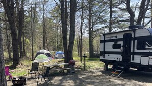 A campsite with tents, a table, chairs, and a camper. - NEW 2025 RV, 1 Bedroom WiFi AC in Serene Winterport with Coast and Bangor nearby (Winterport)