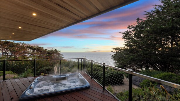 Eine Holzterrasse mit Whirlpool und Blick auf eine malerische Küstenlandschaft.