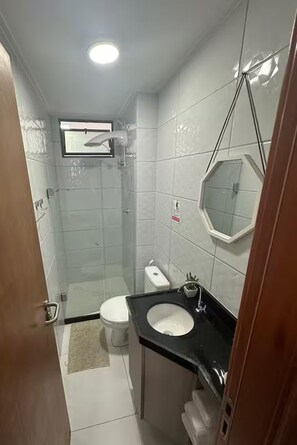 Bathroom features a glass-enclosed shower, toilet, and sink with a black countertop.
